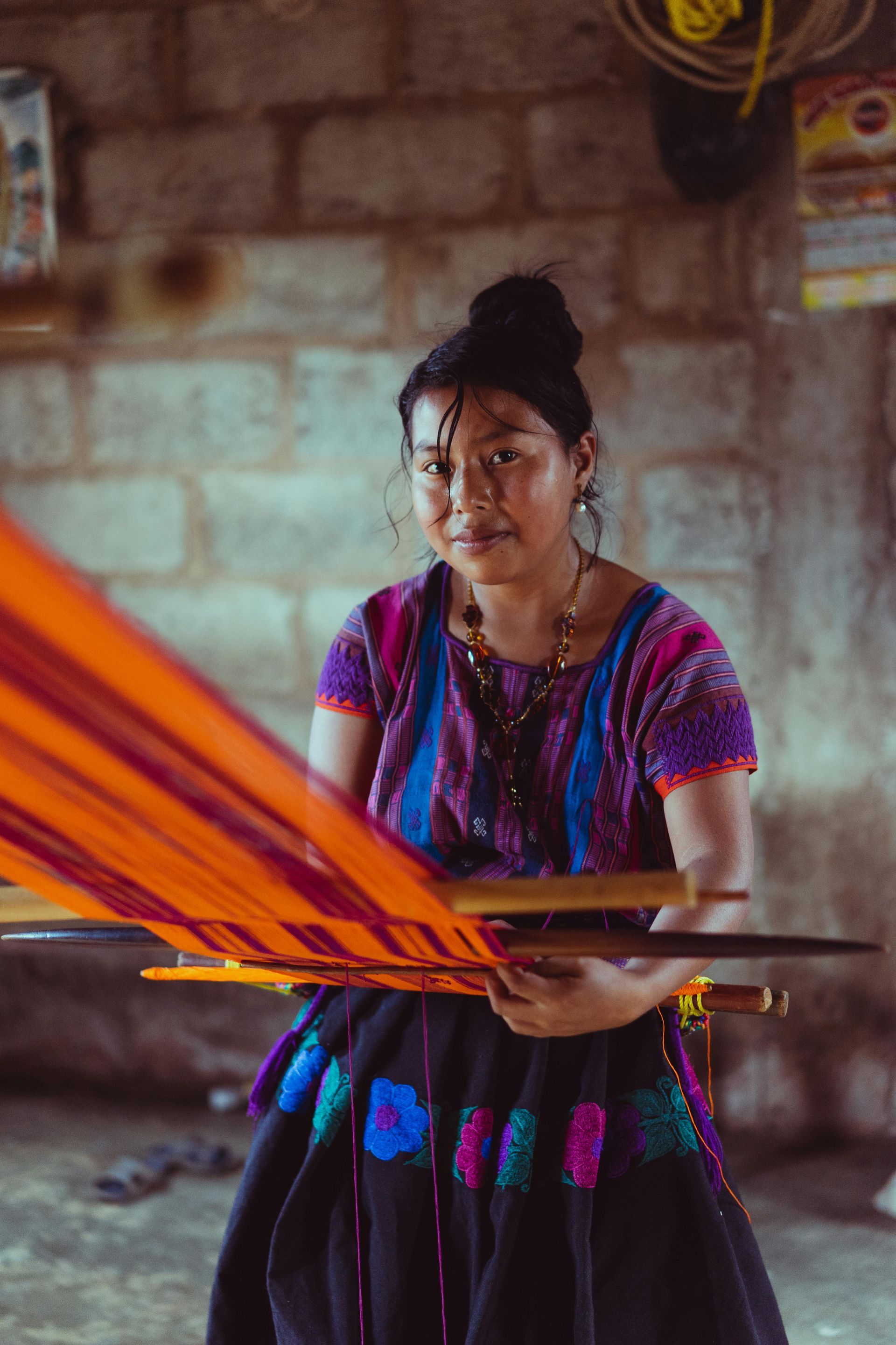 Una mujer con un vestido tradicional está tejiendo una hamaca.