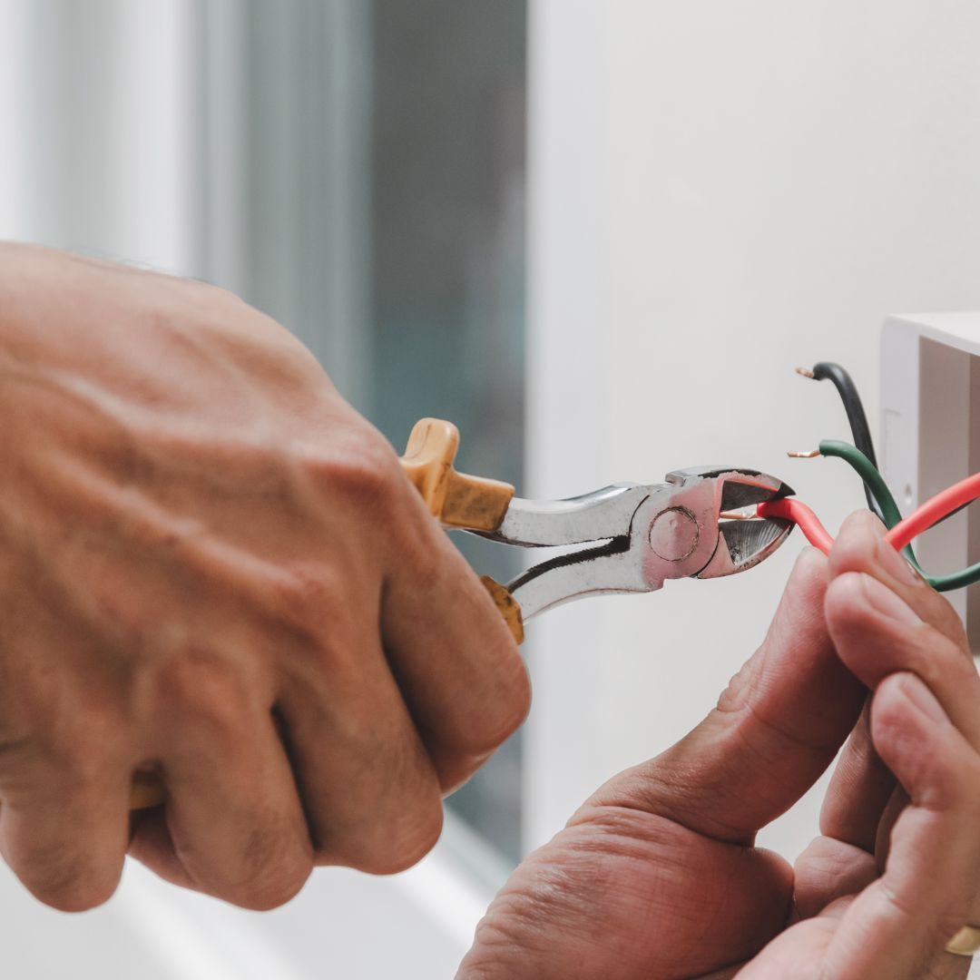A person is working on a light switch with a pair of pliers.