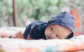 A baby wearing a hoodie is laying on a blanket.