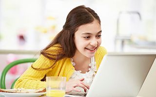 A young girl is sitting at a table using a laptop computer.