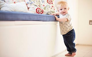 A baby is standing on a bench in a living room.