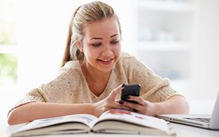 A young woman is sitting at a table with a book and a cell phone.