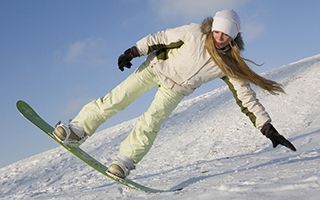 A woman is riding a snowboard down a snow covered hill.