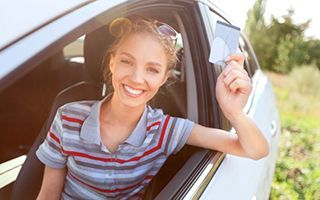 A woman is sitting in a car holding a credit card.