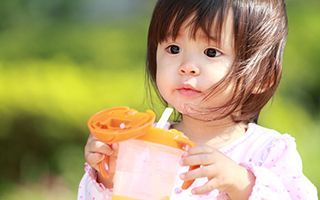 A little girl is drinking from a cup with a straw.