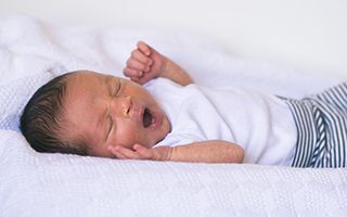 A newborn baby is laying on a bed with his mouth open.