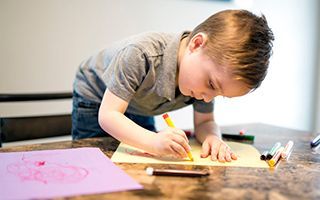 A young boy is sitting at a table drawing with markers.