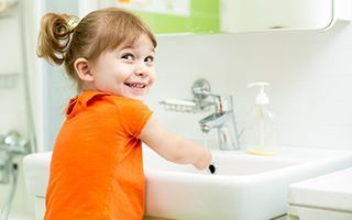 A little girl is washing her hands in a bathroom sink.