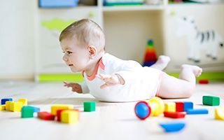 A baby is crawling on the floor surrounded by toys.