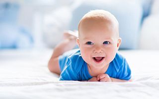 A baby is laying on his stomach on a bed and smiling.