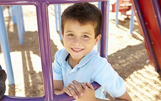 A young boy is smiling while playing on a playground.