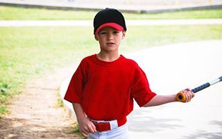 A young boy in a red shirt is holding a baseball bat.