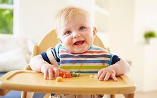 A baby is sitting in a high chair eating vegetables.