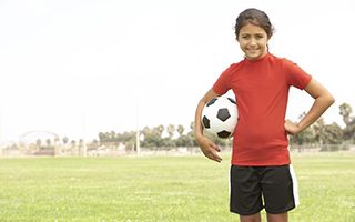 A young girl is holding a soccer ball on a field.