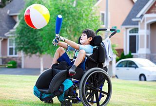 A young boy in a wheelchair is playing with a beach ball and a baseball bat.