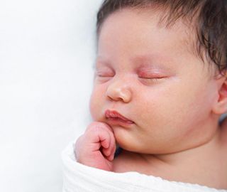 A newborn baby is wrapped in a white blanket and sleeping.