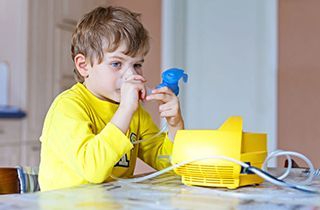 A young boy is sitting at a table using an inhaler.