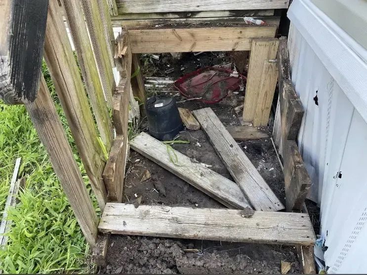Damaged wooden steps and supports beneath a white structure; debris and dirt visible.