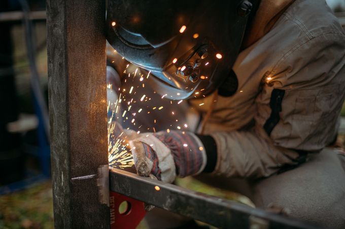 Welder in protective gear, welding metal with bright sparks in outdoor setting.
