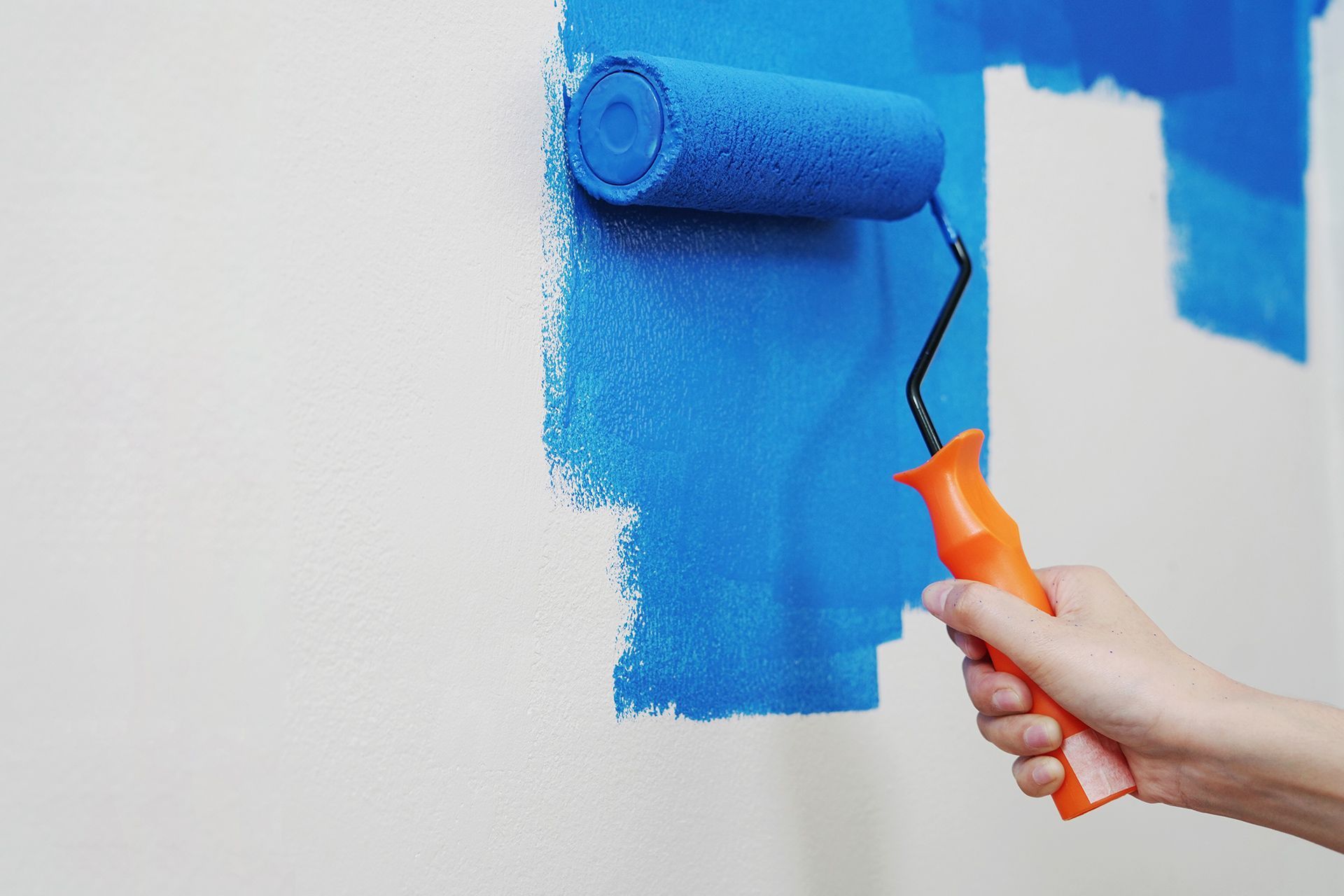 A hand using a roller to paint a wall with vibrant blue paint.