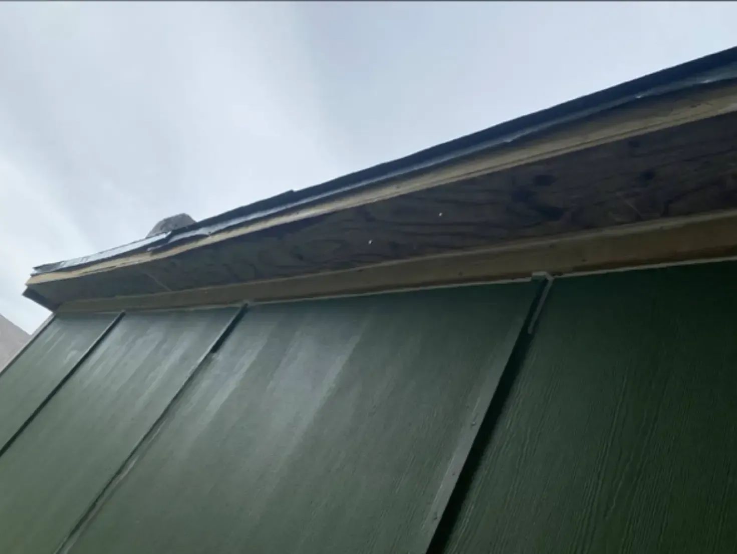 Green siding with a brown roof edge against a cloudy sky.