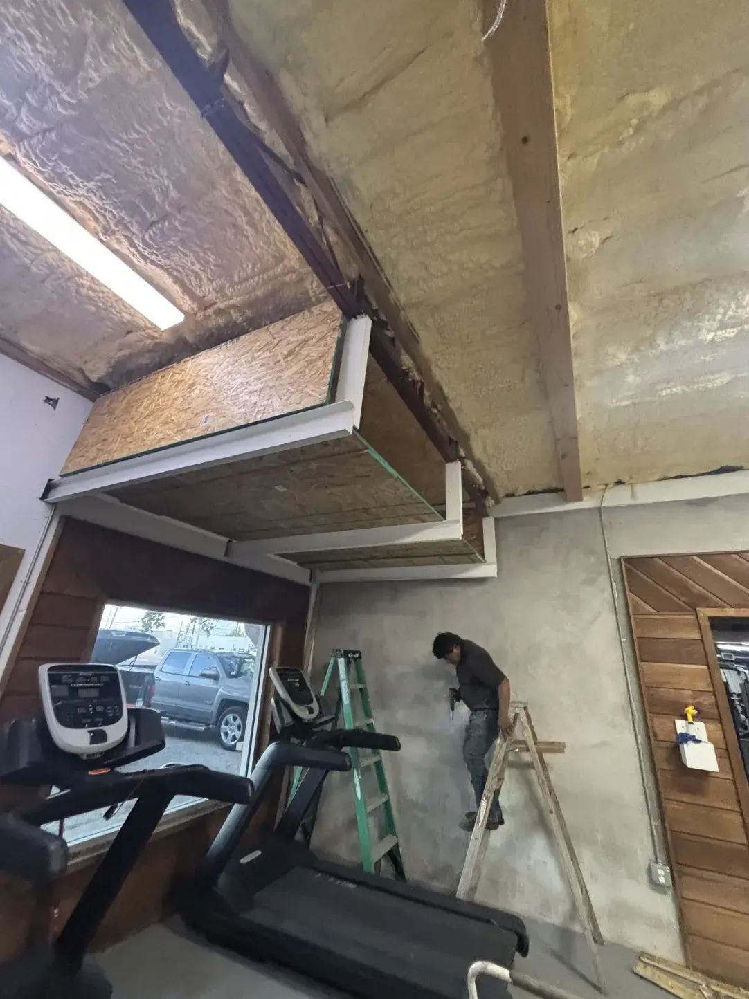 Gym interior with treadmill, construction in progress on the ceiling, a person on a ladder working.