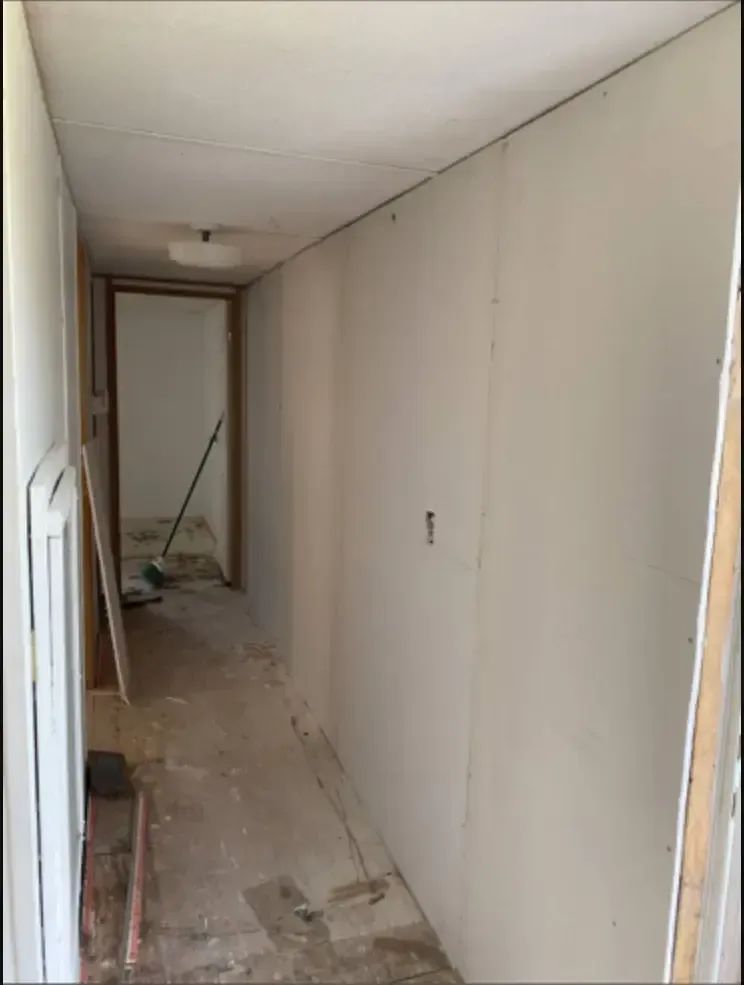 Hallway under construction: drywall installed on walls and ceiling, debris on floor, door frames visible.