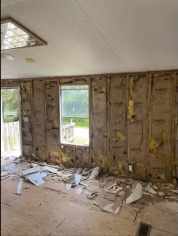 Interior room with damaged walls and debris on the floor, window visible.