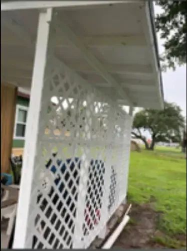 White lattice fence on a porch, with a green grassy background. Overcast day.