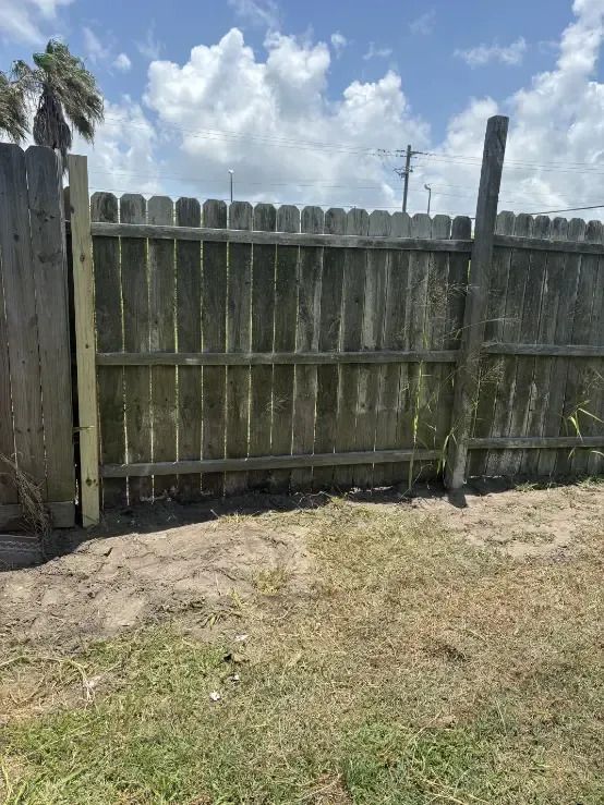 Weathered wooden fence on grass, with a new wooden post. Bright sky in background.