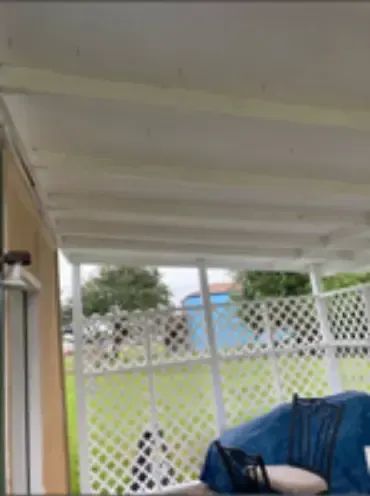 Covered patio with white lattice fence overlooking a grassy yard with a blue building.