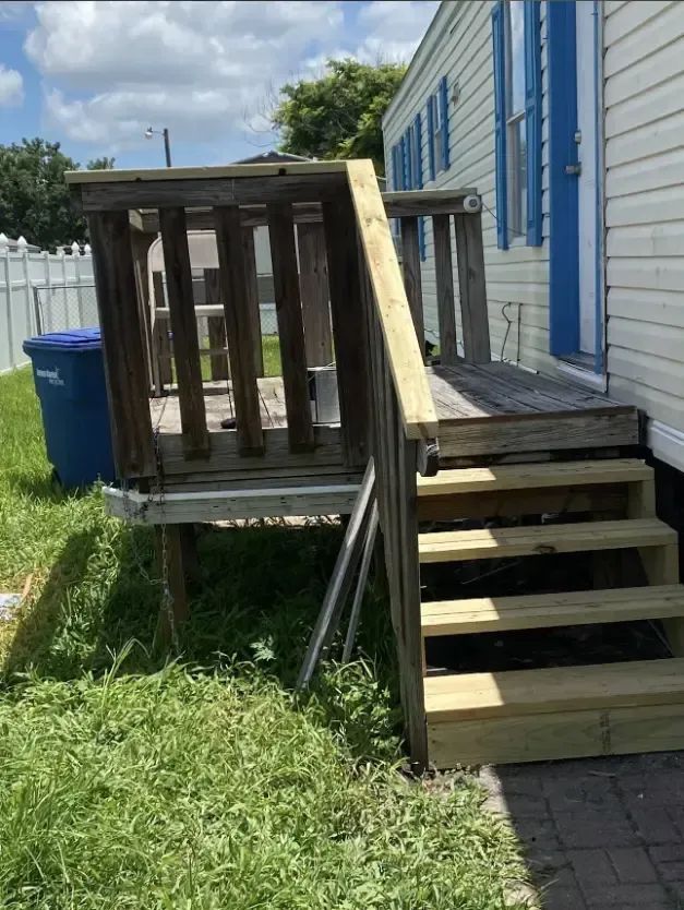 Wooden porch with stairs, railing, and a blue door. Steps are new, and the deck looks aged.