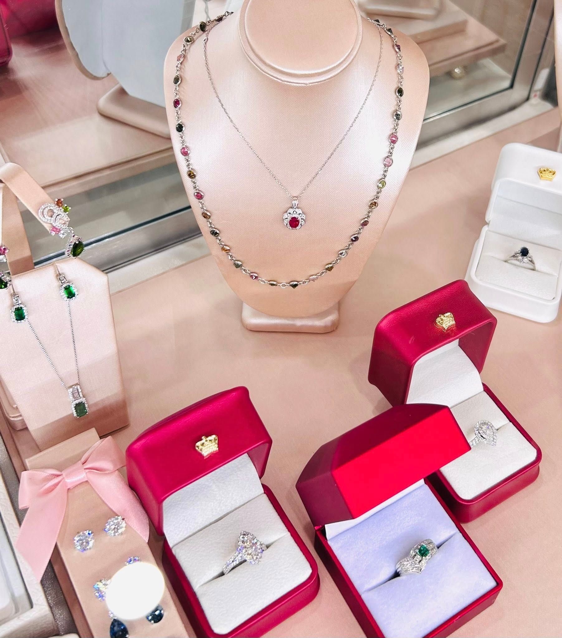 Jewelry display: necklaces, rings in red boxes, earrings, set against a pink surface.