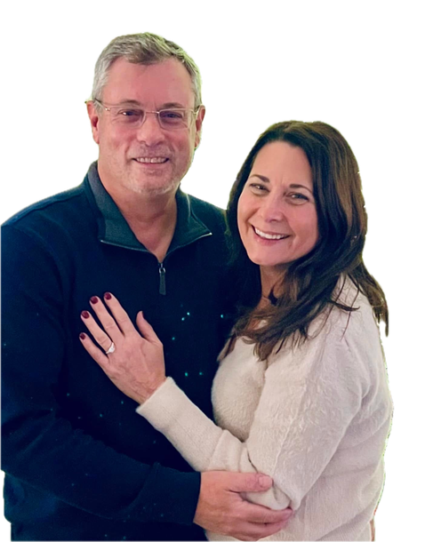 Couple embracing, smiling; woman's hand with ring on man's chest. Indoors, white background.