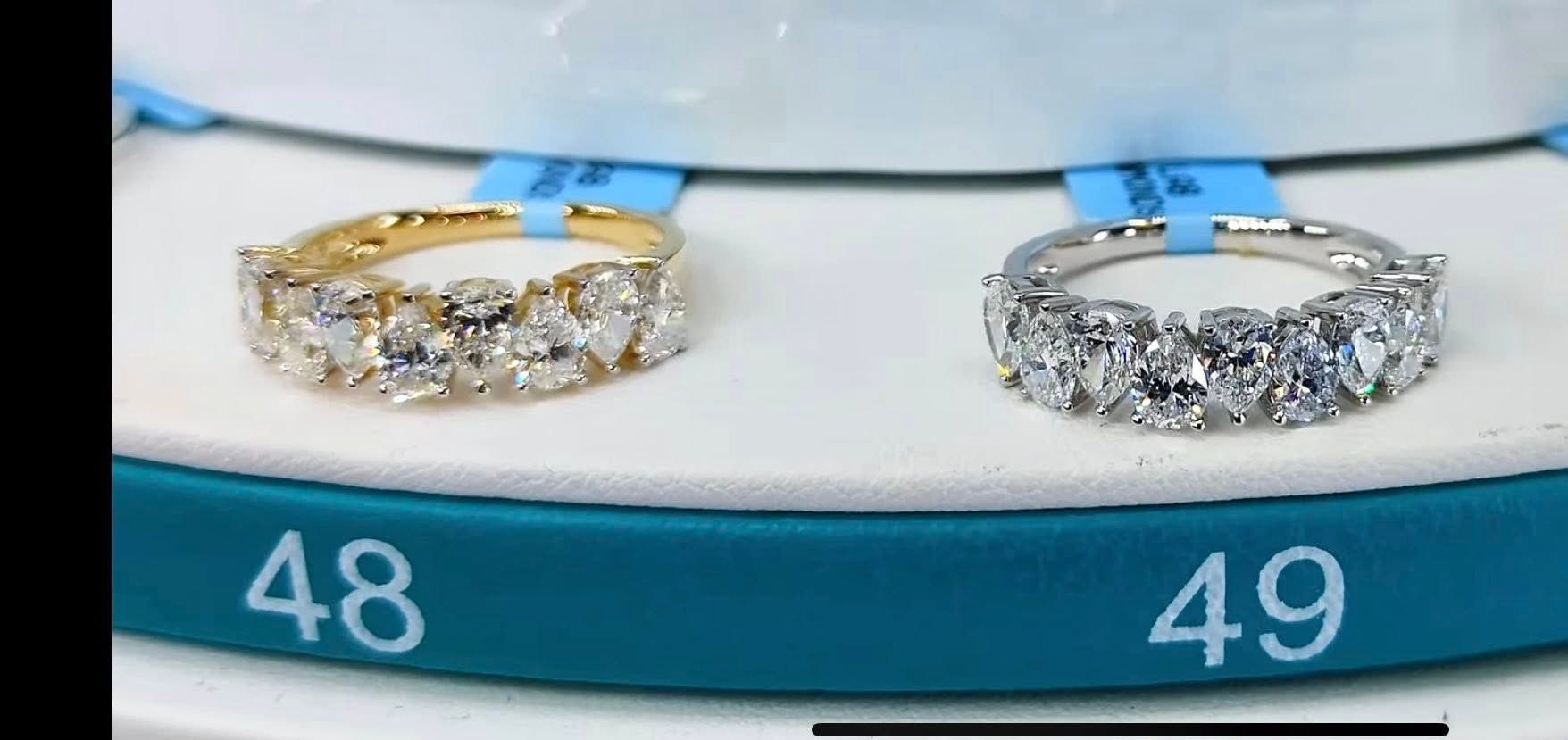 Two diamond rings, one gold, one silver, displayed on a teal surface with size labels 