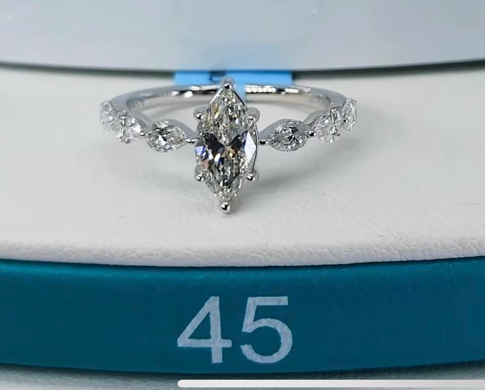 Diamond ring with a marquise-cut center stone and smaller stones on the band, set on a white and teal surface.