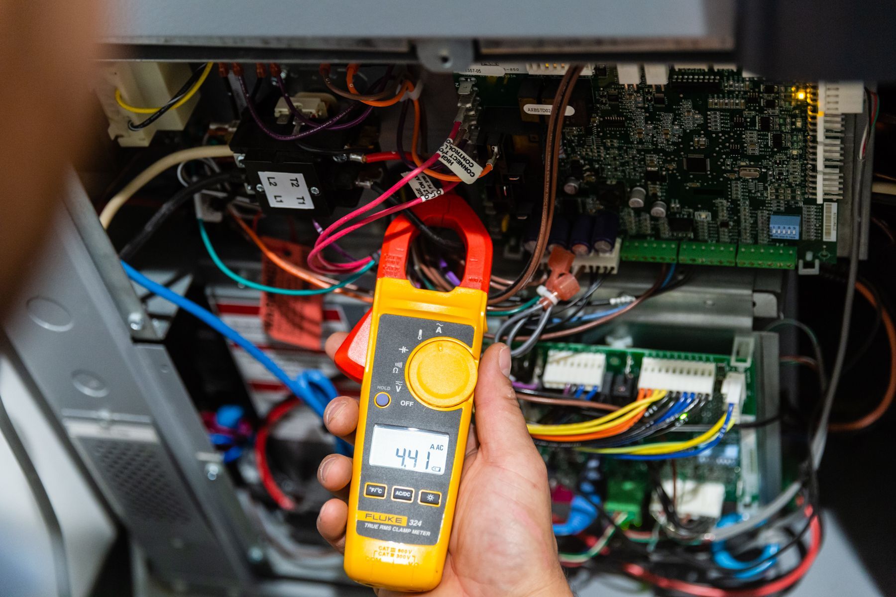 A person is holding a clamp meter in front of a computer.