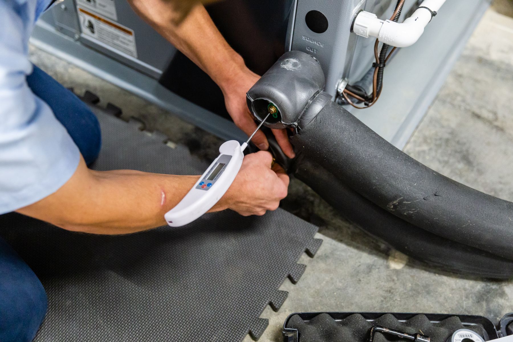 A man is using a thermometer to check the temperature of a pipe.