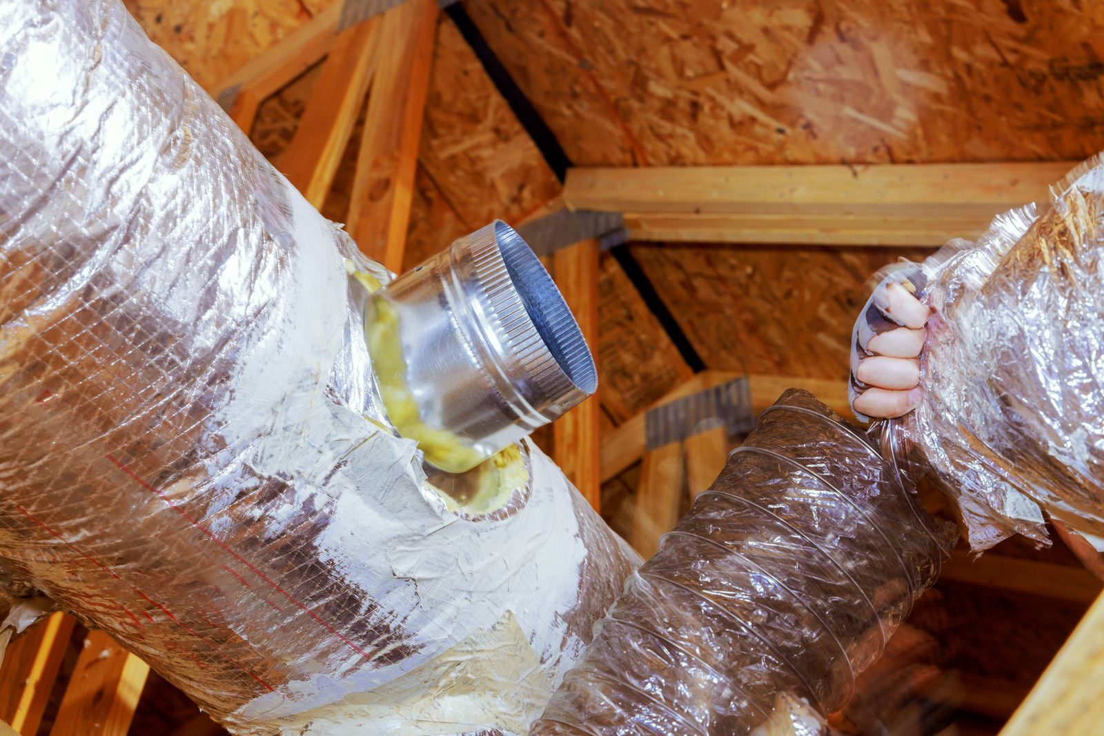 A person is working on a duct in the attic of a house.