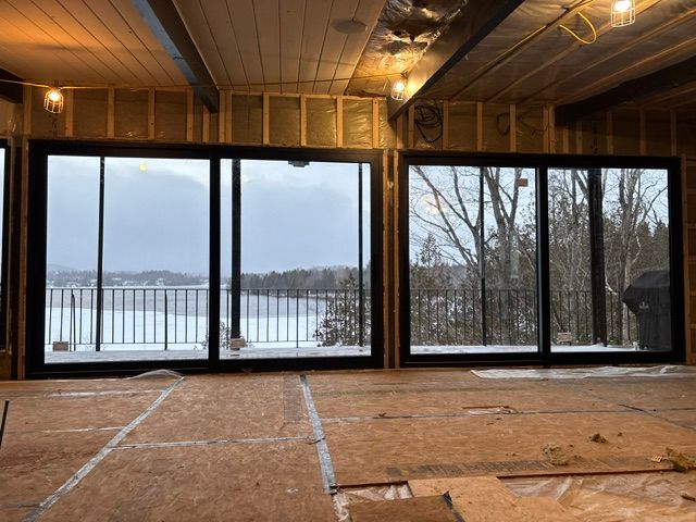 Deux portes coulissantes en verre à cadre noir donnent sur un paysage enneigé depuis un intérieur inachevé.
