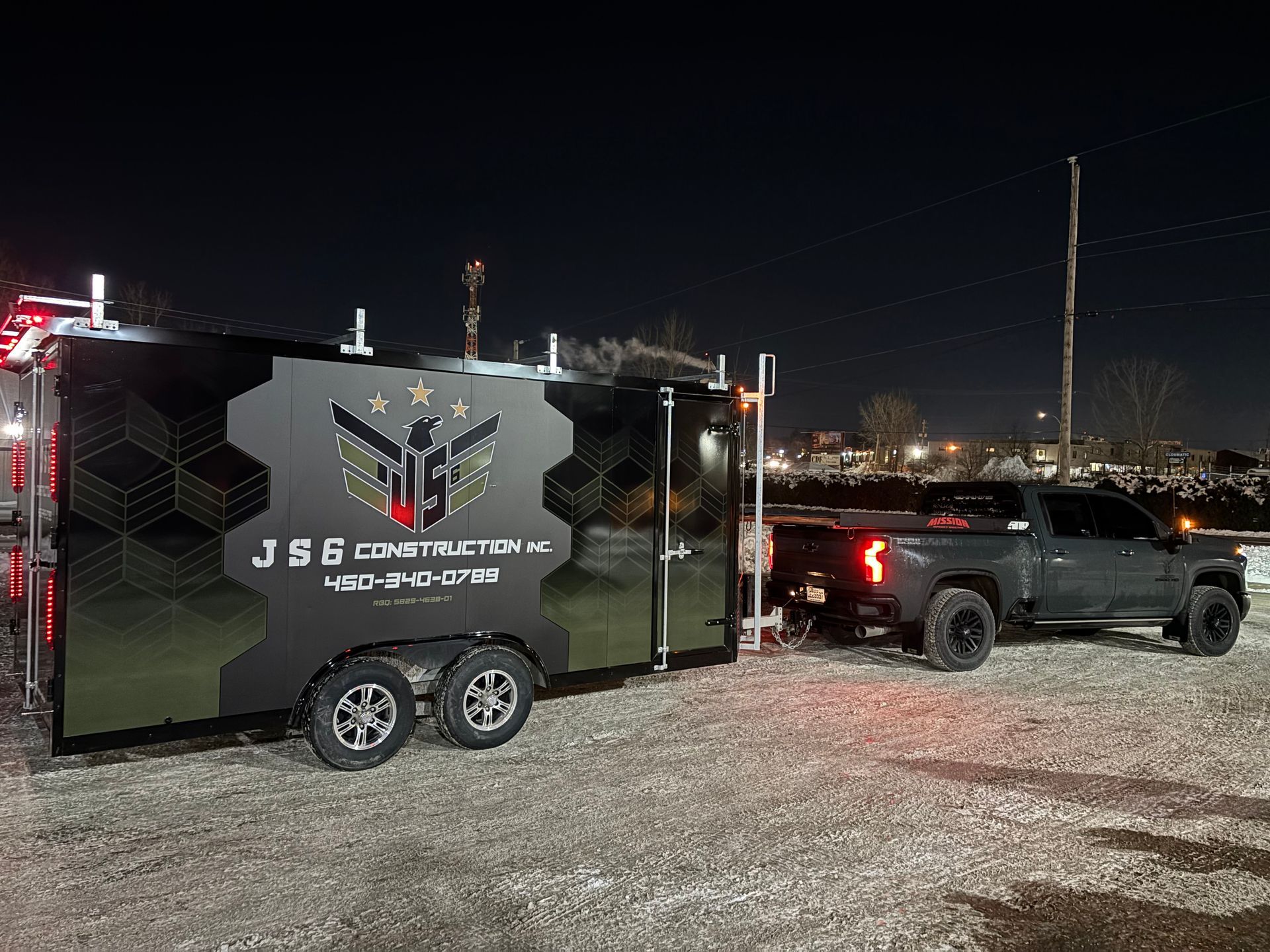 Un camion tractant une remorque de nuit ; la remorque porte le logo d'une entreprise de construction sur le côté.