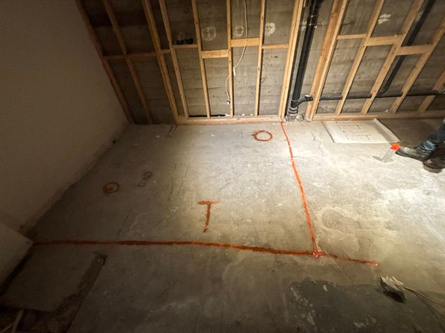 Sol en béton avec marquages ​​orange et charpente en bois apparente ; travaux en cours.