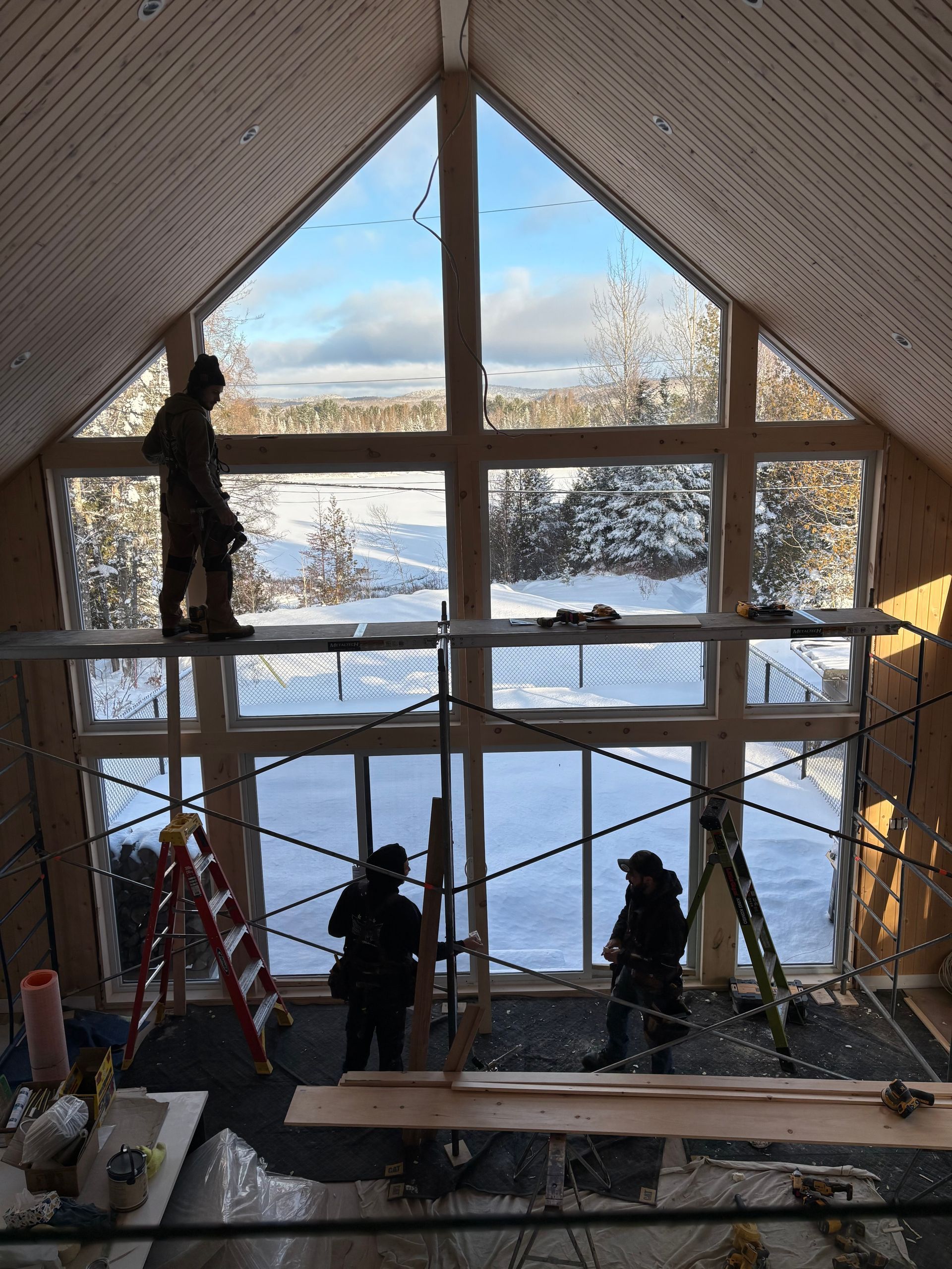 Des ouvriers du bâtiment installent une grande fenêtre donnant sur un paysage enneigé.