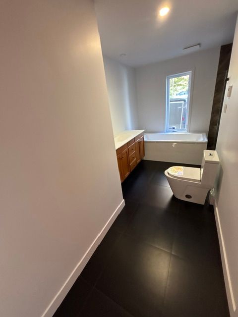Salle de bains moderne avec sol carrelé noir, murs blancs, meuble-lavabo en bois et toilettes.