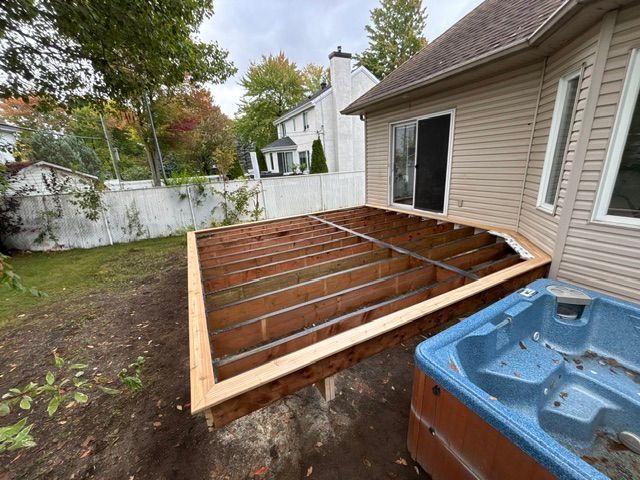 Terrasse en bois partiellement construite à côté d'une maison et d'un jacuzzi bleu.