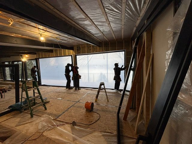 Des ouvriers du bâtiment installent de grandes fenêtres dans une pièce aux poutres apparentes.