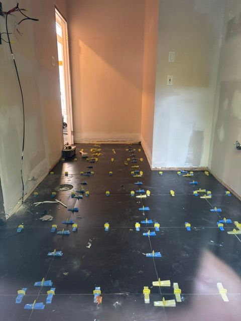 Intérieur en cours de réalisation avec sol carrelé foncé, clips de nivellement bleus et jaunes visibles.