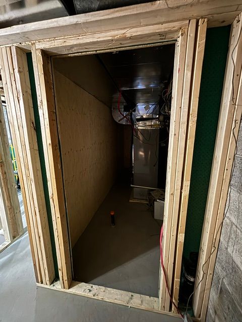Porte encadrée donnant sur une pièce étroite au sous-sol avec des conduits d'aération apparents et des murs non finis.