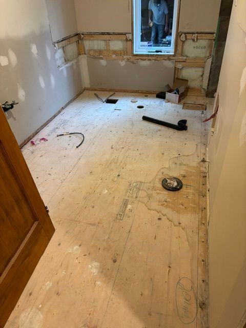 Salle de bains en rénovation ; plancher apparent, murs partiellement finis, installations sanitaires.