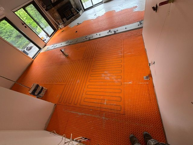 Sol orange avec système de chauffage installé, prêt à être carrelé, dans une pièce avec fenêtres et murs blancs.